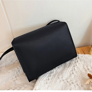 Détail du petit sac bandoulière en similicuir noir sur fond de textile en dentelle blanche