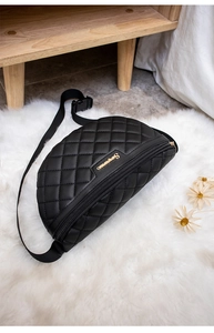 Detail der schwarzen gesteppten Bauchtasche mit goldenem Logo auf Plüschteppich