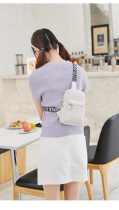 Detail of white quilted chest bag with wide lettered strap and gold zipper pendant