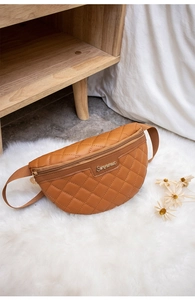 Detail der braunen Stepp-Brusttasche mit goldenem Metalllogo und Gurtband