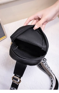 Detail view of the black round cross-body bag interior and wide logo-woven shoulder strap