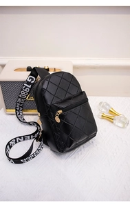 Detail of black quilted chest bag with golden hardware and patterned strap on a desk