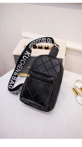 Detail of black quilted chest bag with golden zippers and branded woven strap on a white table