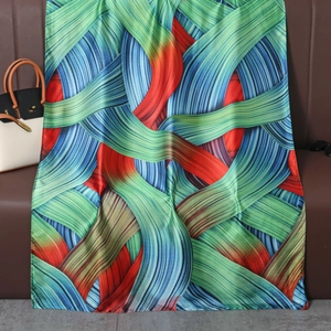 Elegant long silk-like scarf with colorful geometric lines draped next to a handbag