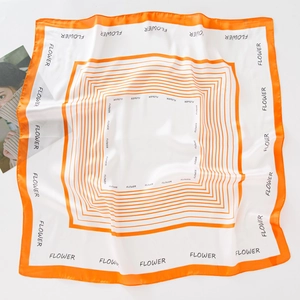 Détail d'un foulard en soie avec bordure orange et imprimé de motifs floraux blancs