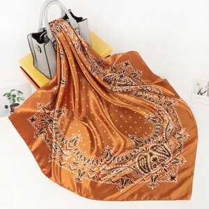 Close-up of a satin paisley scarf with orange tones tied to a grey handbag as an accessory