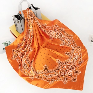 Detail of orange paisley satin scarf draped over a leather bag with glossy finish