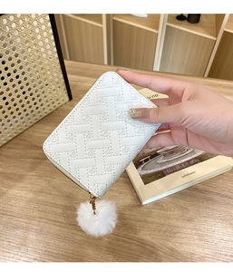 Close-up of white woven leather coin purse with heart print and soft pompom charm