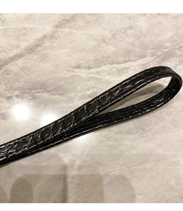 Détail de la texture cuir gaufré crocodile noir sur la dragonne d'un long portefeuille