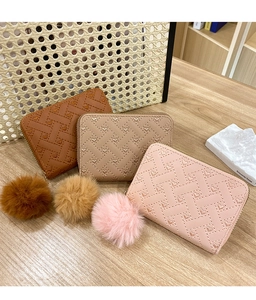 Detailed view of woven heart pattern leather coin purses with plush pom-poms on wood
