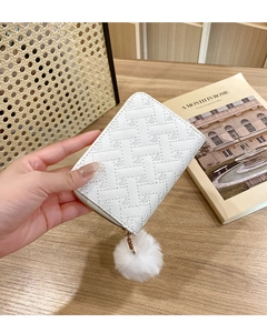 Close-up of white heart-quilted coin purse with fluffy pompom detail in a lifestyle setting