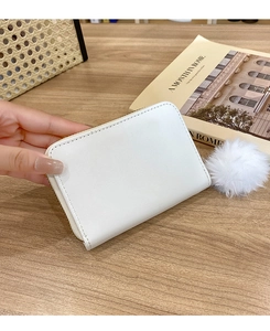 White quilted mini wallet with plush ball charm held by hand on wooden background