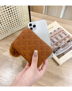 Detailed view of brown quilted card wallet with pompom next to a smartphone