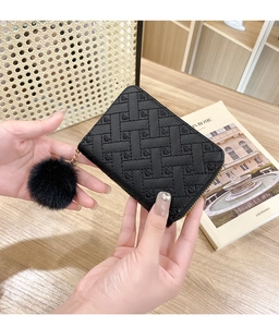 Close-up of black heart-quilted coin purse with golden zipper and faux fur pompom detail