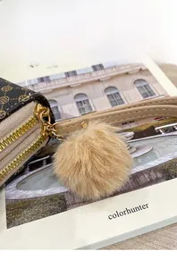 Detailed close-up of a long printed wallet with a soft faux fur pompom charm and wrist strap