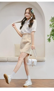 Full body view of a girl wearing a white lace shirt and yellow checkered A-line skirt