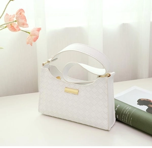 Detail of white baguette underarm bag with woven texture and gold metal buckle