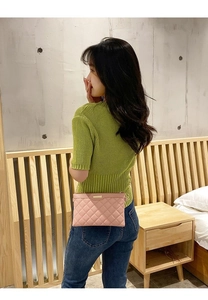 Sac bandoulière rose matelassé avec plaque dorée porté par un modèle dans une chambre