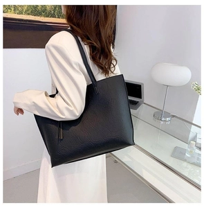 Vue détaillée du grand sac cabas noir texturé porté par un mannequin dans un bureau