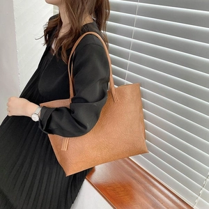 Grand sac cabas marron à pompons porté par un mannequin dans une robe noire chic