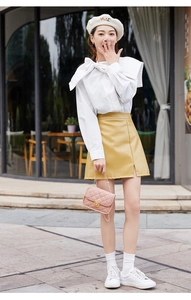 Detailed view of a white bow-knot shirt paired with a mustard yellow faux leather mini skirt