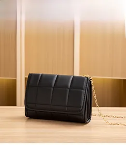 Detail of black quilted chain bag with gold metal strap on a light wood surface