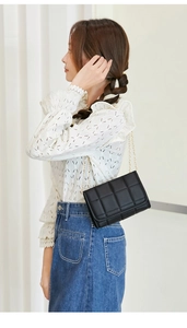 Detailed side view of a black quilted crossbody bag with a slim gold chain strap on a model