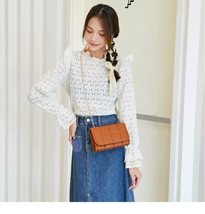 Close-up of a brown quilted flap bag with a gold chain strap worn with a denim skirt