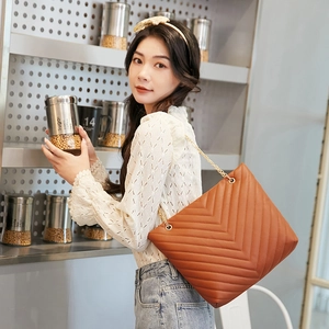 Detail of brown V-quilted tote bag with gold chain strap worn in a modern kitchen