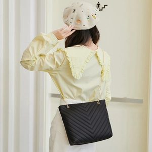Detailed view of black V-quilted shoulder bag with gold chain strap on stylish model