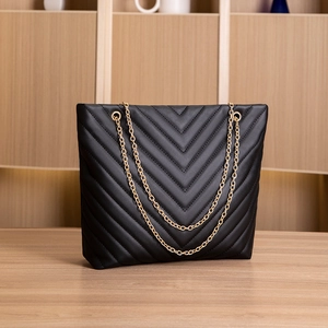 Detail of black V-quilted faux leather tote with elegant golden metal chain straps