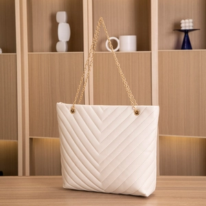 Detail of chevron quilted cream tote bag with elegant gold chain strap on wooden surface