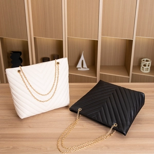 Close-up of black and white V-quilted tote bags with gold chain straps on wood surface