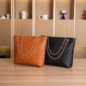 Detailed view of V-quilted faux leather tote bags in brown and black with gold chains
