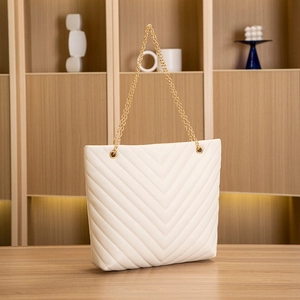 Detail of white quilted leather tote bag with V-shaped stitching and golden chain handles