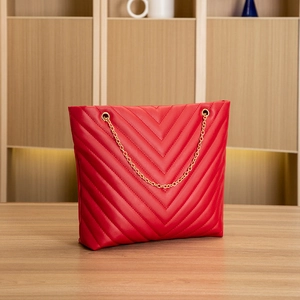 Detail view of red V-quilted faux leather tote with elegant gold chain shoulder straps
