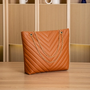 Detail of brown tote bag with V-shaped chevron quilting and golden chain straps