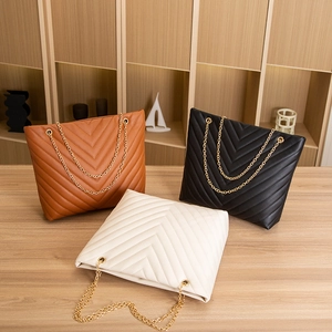 Trio of V-quilted faux leather tote bags in brown, black, and white with gold chain straps