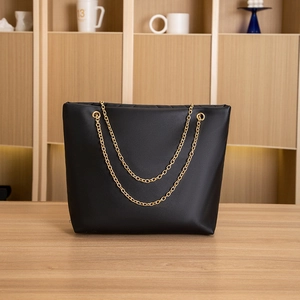 Front view of black tote bag with V-shaped embroidery and golden chain straps