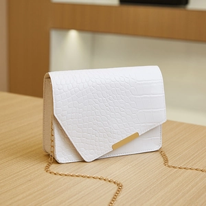 Elegant white crocodile embossed mini crossbody bag with gold chain strap on table