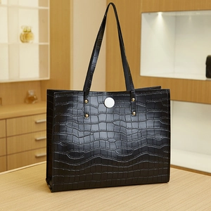 Close-up of black crocodile pattern tote bag with golden rivets and white buckle detail