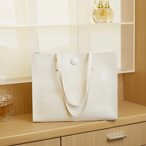 Detail of white tote bag showing faux crocodile leather texture and magnetic buckle closure