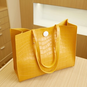 Detail of yellow tote bag featuring crocodile embossed texture and white round buckle