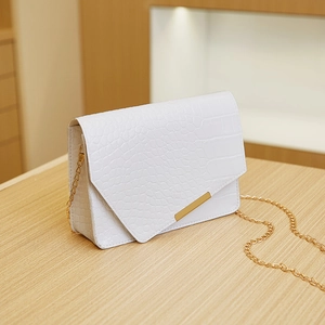 Close-up of white crocodile pattern shoulder bag with a gold chain strap on wooden surface