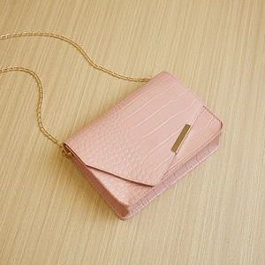 Detail of pink croc-embossed square bag with elegant gold hardware and chain strap