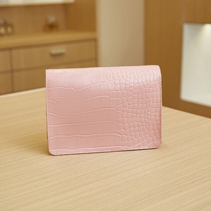 Detail of pink crocodile embossed leather envelope bag with premium stitching on wooden table