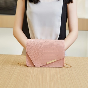 Detail of pink croc-textured bag with asymmetric flap and elegant gold chain strap