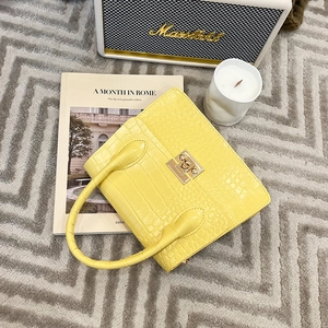 Detail of yellow crocodile embossed leather handbag with gold metal clasp on a gray rug