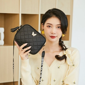 Close-up of black quilted crossbody camera bag with butterfly ornament and wide strap