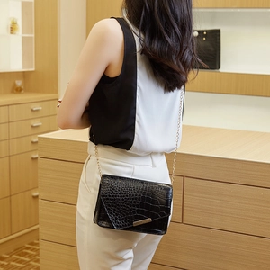 Close-up of black crocodile pattern crossbody bag with gold chain on a female model